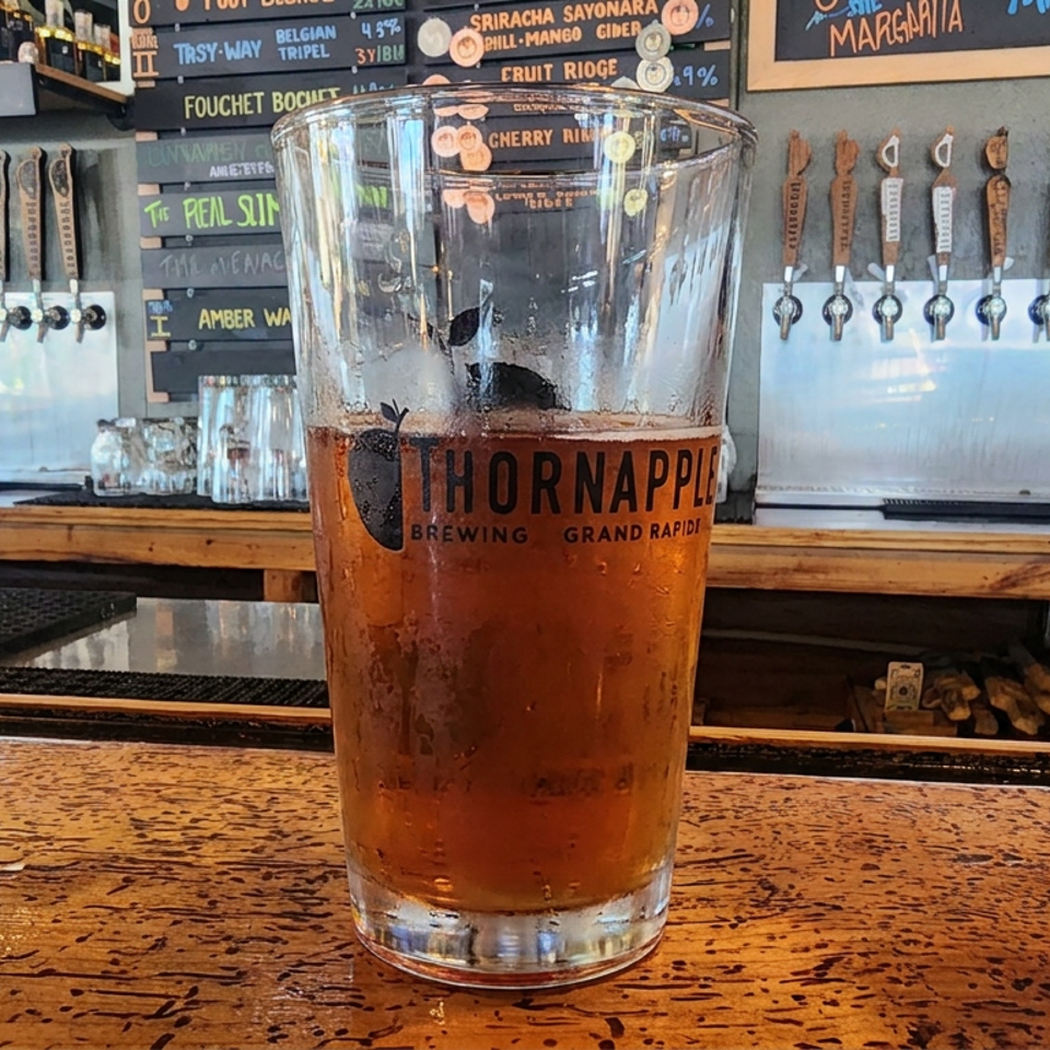 Pint of Thornapple Brewing beer on a wooden bar, with numerous taps and chalkboard beer menus in the background.